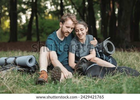 Photo of couple and a dog sitting in forest at summer with backpacks