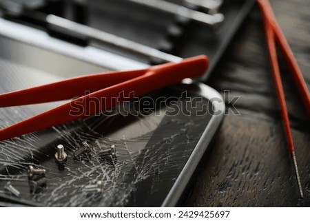 Smartphone with a broken screen and repair tools on the dark background.