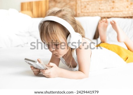 girl plays with smartphone and listens to music on headphones, watches cartoons on phone, online learning, online games