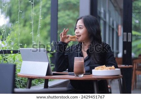 the elegance of a young Asian woman in a candid online meeting snacking in front of a laptop in a cafe