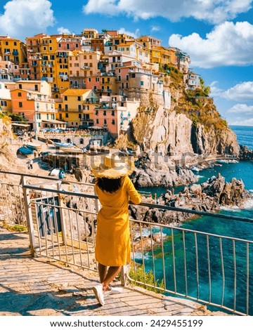 Asian women visiting Manarola in Cinque Terre Italy,beautiful colorful town of La Spezia Liguria one of the five Cinque Terre, woman with hat standing by the ocean during summer in Europe Royalty-Free Stock Photo #2429455199