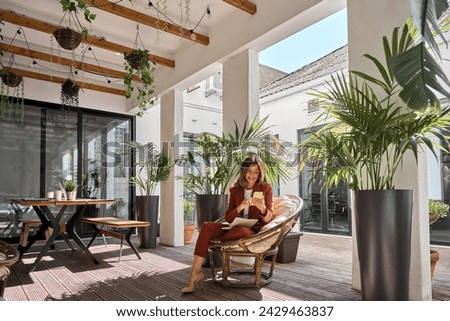 Happy elegant mature middle aged older business woman holding cellphone using mobile cell phone looking at smartphone sitting in comfortable chair in sunny office space with green plants. Royalty-Free Stock Photo #2429463837