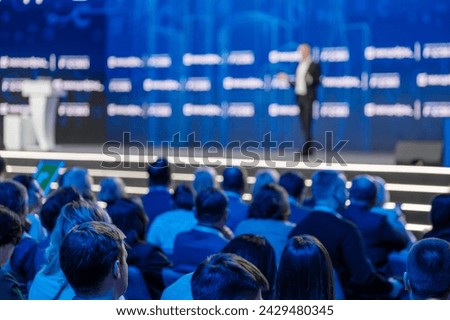 Blurred view of a speaker at a professional conference with an audience in sharp focus listening attentively. Royalty-Free Stock Photo #2429480345