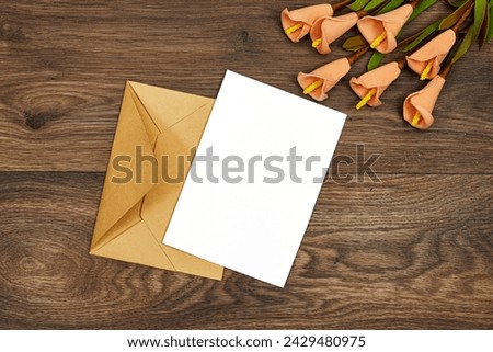 Wedding invitation card mockup and kraft brown paper envelope with orange calla lilies flowers on wood table. Blank card mockup