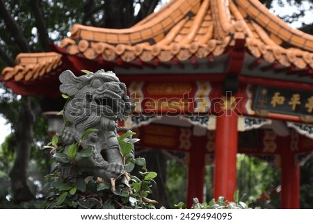 Ancient stone dragon head statue, typical asian fantasy style, with religious ornaments and oriental decorations in garden at taiwanese old spiritual traditional red temple in Taipei, Taiwan, Asia. Royalty-Free Stock Photo #2429494095