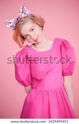 Kids and teenage fashion. A cute blonde teenage girl with a short haircut poses in a pink dress and a lovely headband with floral kitty ears. Pink background. Spring-summer look.
