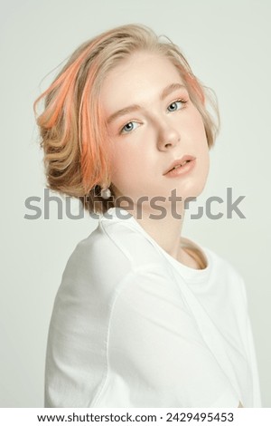 Beauty, style and fashion. A cute teenage girl with a short haircut and blonde hair with orange streaks poses in a white T-shirt on a white studio background. Adolescence. 
