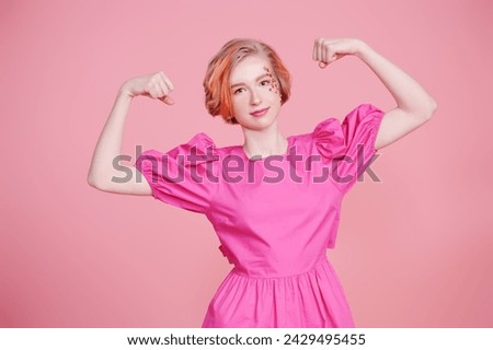 Teenage Fashion. A modern teen girl with a short blonde hair with orange streaks shows strength with flower stickers on her face, wearing a pink dress. Pink background. Spring-summer look. Copy space.