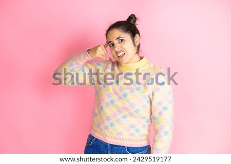 Young beautiful woman wearing casual sweater over isolated pink background confused doing phone gesture with hand and fingers like talking on the telephone
