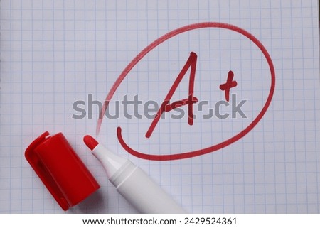 School grade. Red letter A with plus symbol on notebook paper and marker, top view