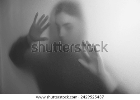Silhouette of ghost behind fabric against light grey background. Black and white effect