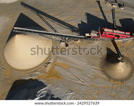 Single red industrial stone crusher machine with prefect cone heaps of sand. Aerial view of industrial machine on a sunny morning. Royalty-Free Stock Photo #2429527639