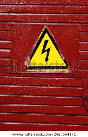 Caution dangerous alert sign. Old door, painted burgundy with thick paint, triangular yellow warning sign with lightning, high voltage, danger