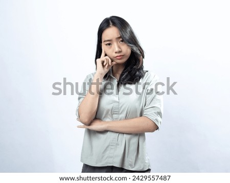 Skeptical Asian Indonesian Chinese woman with arm crossed, pondering, in a silky blouse, against a white backdrop Royalty-Free Stock Photo #2429557487