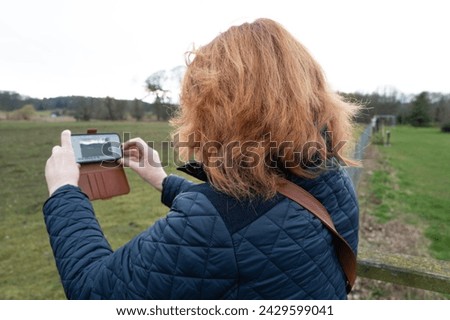 Woman tourist seen using her smart phone to take a landscape image of a wildlife park in the Britain.