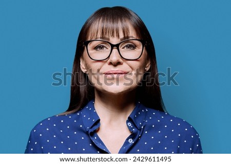Headshot portrait of smiling business mature woman on blue background