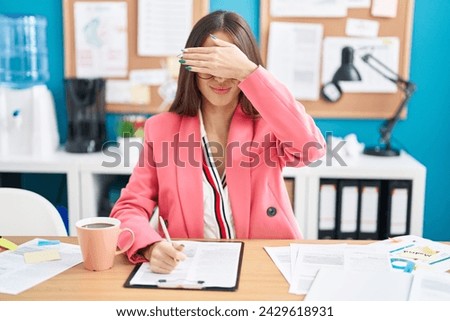 Young hispanic woman working at the office wearing glasses covering eyes with hand, looking serious and sad. sightless, hiding and rejection concept  Royalty-Free Stock Photo #2429618931