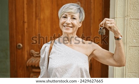 A cheerful mature hispanic woman proudly displays house keys in front of her new home's wooden door, symbolizing ownership and a fresh start Royalty-Free Stock Photo #2429627665