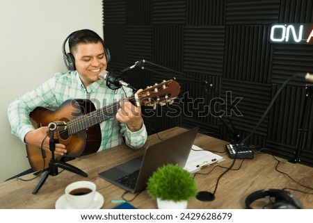 Cheerful happy man enjoying playing his music with a guitar while smiling in the soundproof recording studio