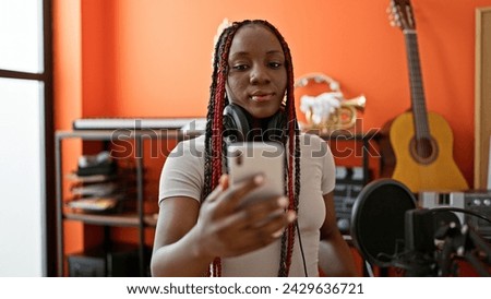 Beautiful african american woman musician, in braids and headphones, captures a serious selfie on her smartphone in an intimate music studio setting