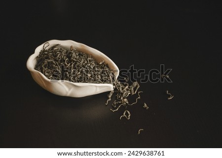 A white bowl filled with terrestrial plant green tea leaves resting on a black table, creating a beautiful still life photography composition in darkness