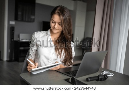 Young woman using laptop in home workplace, writing notes, female student learning and watching online webinar or listening audio course, e-learning education concept. High quality photo