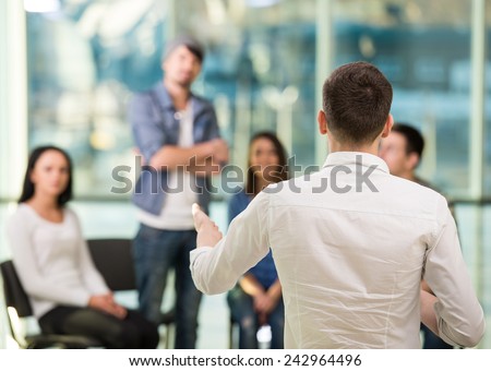 Young man is sharing his problems with people. View of man is telling something and gesturing while group of people are sitting in front of him and listening.