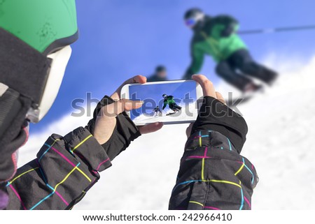 A young girl by mobile phone photographed two skiers