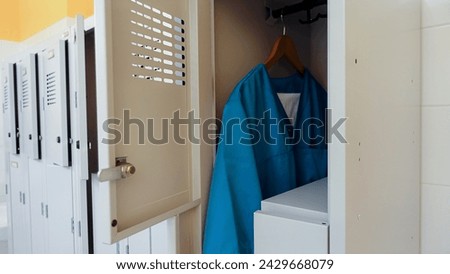 Open metal lockers in the locker room. A nurse's clothes, turquoise smocks and trousers, are hanging on a hanger. Concept of acute shortage of care staff and doctors in hospitals and nursing homes.    Royalty-Free Stock Photo #2429668079