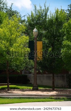Light pole banner welcoming flyer near lush green tree, brick walkway in large Texas college campus, ample green space, education and landscaping concept. USA