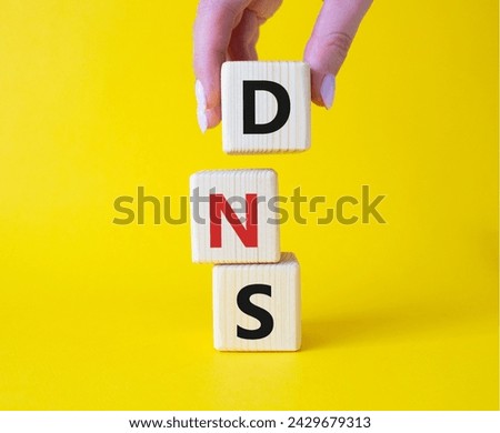 DNS -Domain Name Server - Consumer Price Index symbol. Concept word DNS on wooden cubes. Businessman hand. Beautiful yellow background. Business and DNS concept. Copy space.