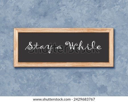 Close up image of a sign on a wall that reads Stay a While. Royalty-Free Stock Photo #2429683767