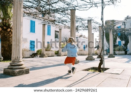 Little girl walks between pergola columns in a garden near a three-story building Royalty-Free Stock Photo #2429689261