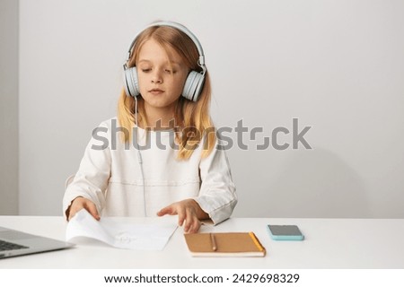 Happy young girl using a laptop for elearning and online games at home, enhancing her education and digital skills With a smile on her face, she sits at a table with notebooks and a writing notebook,