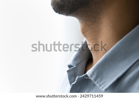 Unknown young man neck and shirt collar. Bearded guy cropped close up on copy space. Male laryngeal cartilage, Adams apple, sore throat, pharyngitis, laryngitis, prominent thyroid cartilage side view Royalty-Free Stock Photo #2429711459