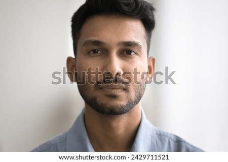 Close up of unsmiling Indian bearded guy standing indoor staring at camera. Man having attractive appearance, looks confident and serious. Millennial generation person, businessman head shot portrait Royalty-Free Stock Photo #2429711521
