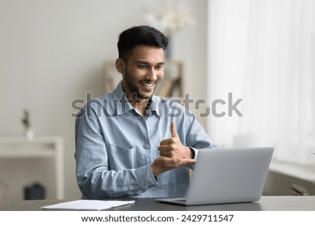 Young smiling Indian man with hearing disability sit at desk with laptop, make video call, take part in virtual meeting or online class showing hands gestures, lead communication using sign language