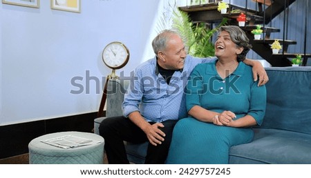 Indian happy middle aged old husband wife sitting on comfy sofa couch making funny communication at indoor home. Smiling older senior couple enjoying romantic talking together summer vacation holiday  Royalty-Free Stock Photo #2429757245