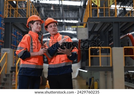 Male and Female engineer with orange safety vest and hard hat work in train garage  Royalty-Free Stock Photo #2429760235