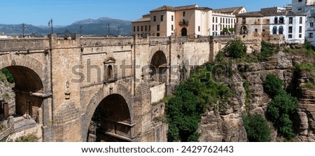 An ancient stone bridge arches majestically over a chasm, connecting two parts of an old town Ronda against a backdrop of rolling hills and clear skies. Royalty-Free Stock Photo #2429762443