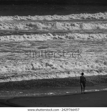 Black and white photo of a silhouette of one person standing on a beach in rough seas