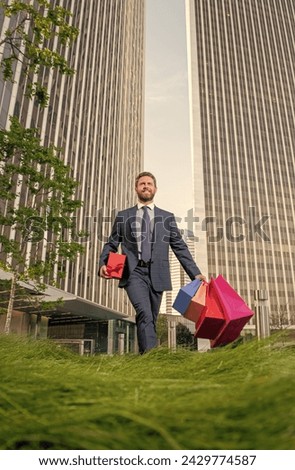 cheerful man in formalwear with shopping bags and present box walk outside the office, birthday.
