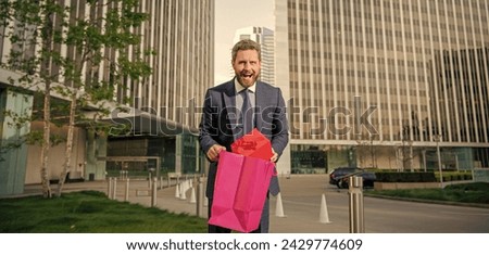 surprised entrepreneur in suit holding shopping bag and giftbox outside the office, boxing day.