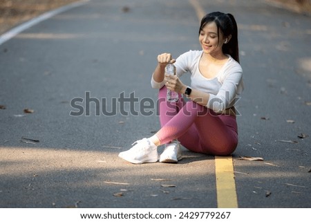 Young woman takes a break and drinks a water bottle after exercising in the park.