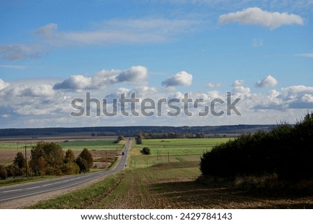 Asphalt road, field and forest with sky and clouds. Landscape of the Central Russian plain in early autumn