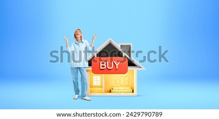 Smiling young European woman standing near house with buy sign over blue background. Concept of real estate purchase