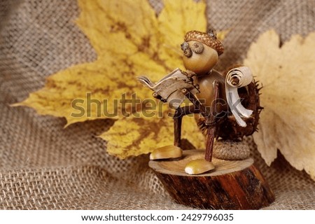 Autumn little man sitting on a stump on a background of yellow leaves and burlap and reading a book. Handmade figurine. Students' works and ideas. There is space for text in the photo.