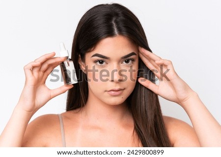 Young Brazilian woman isolated on white background holding a serum. Close up portrait