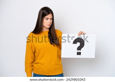 Young Brazilian woman isolated on white background holding a placard with question mark symbol