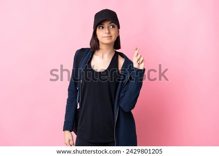 Young sport woman with sport bag isolated on pink background with fingers crossing and wishing the best